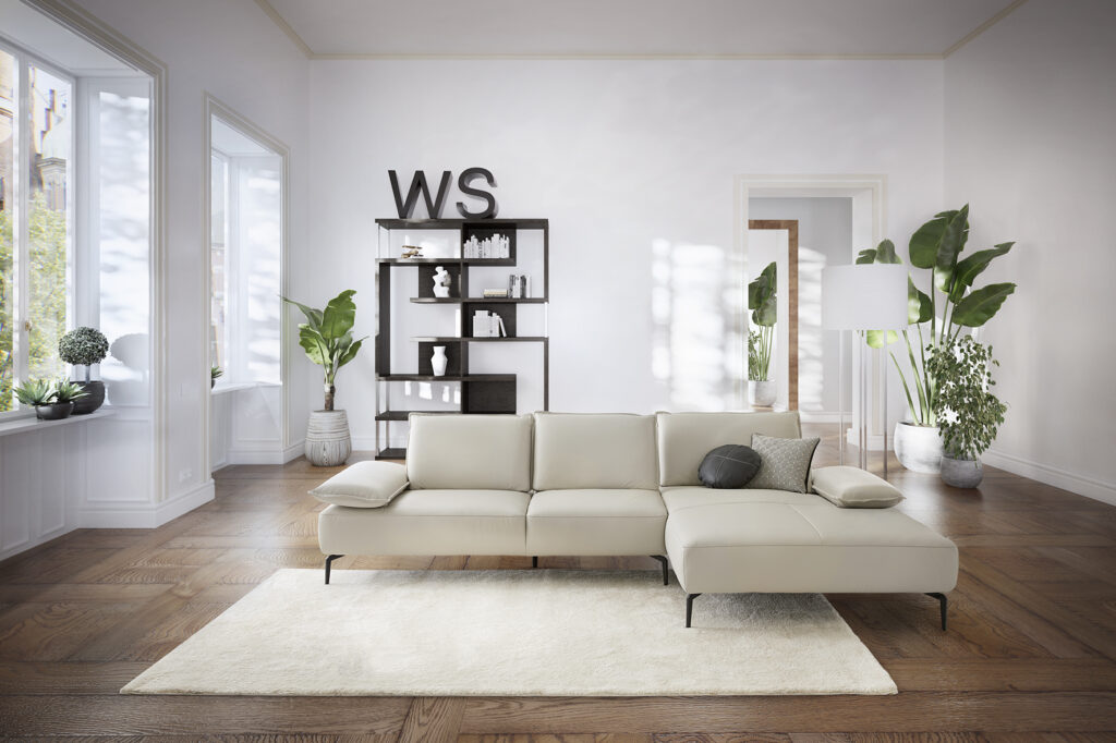 Sofa-Longchair-Kombination Modell 16568 in einer Raumszene bei Tageslicht, in weißem Leder, mit schwarzen Metallfüßen. Frontansicht, Business-Style. Wohnstil hell und kühl, mit vielen Grünpflanzen und minimalistischer Einrichtung. Dunkler Holzboden, weiße Wände, hohe große Fenster, heller Teppich.